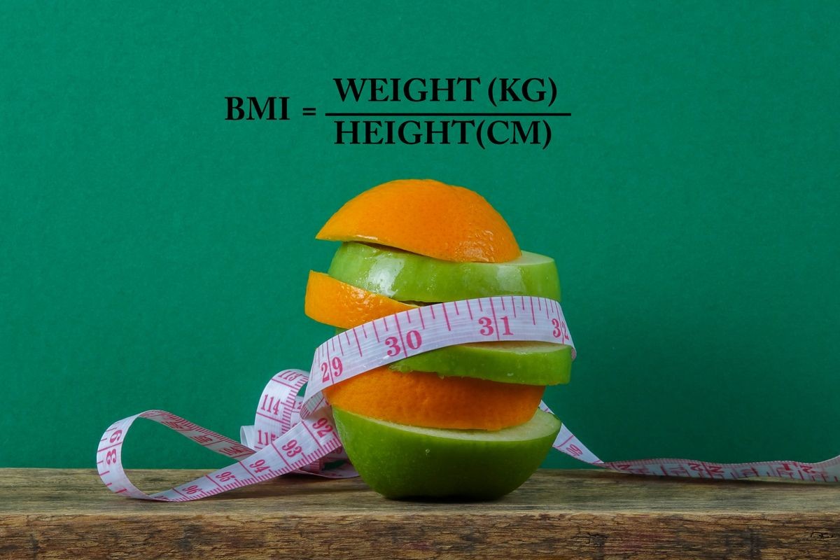 A conceptual fruit of fitness with green apple and orange and a measuring tape with BODY MASS INDEX (BMI) formula.